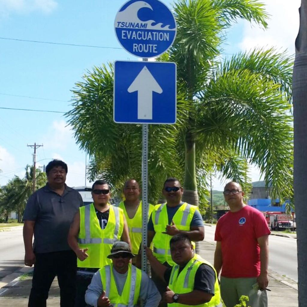 CNMI residents standing in front of tsunami evacuation sign.